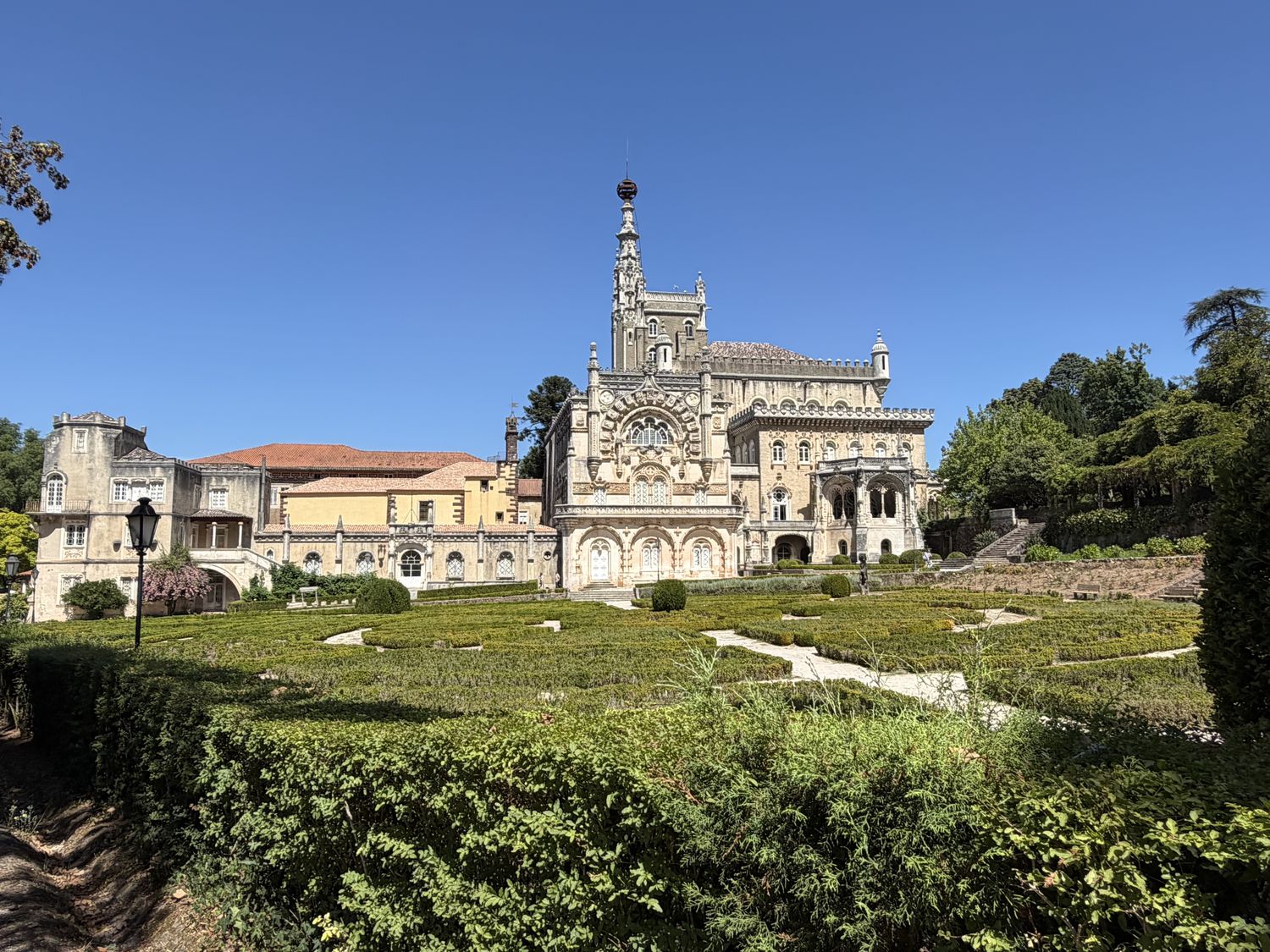 The neo-Manueline Buçaco Palace above formal box-hedge gardens under a clear blue sky.